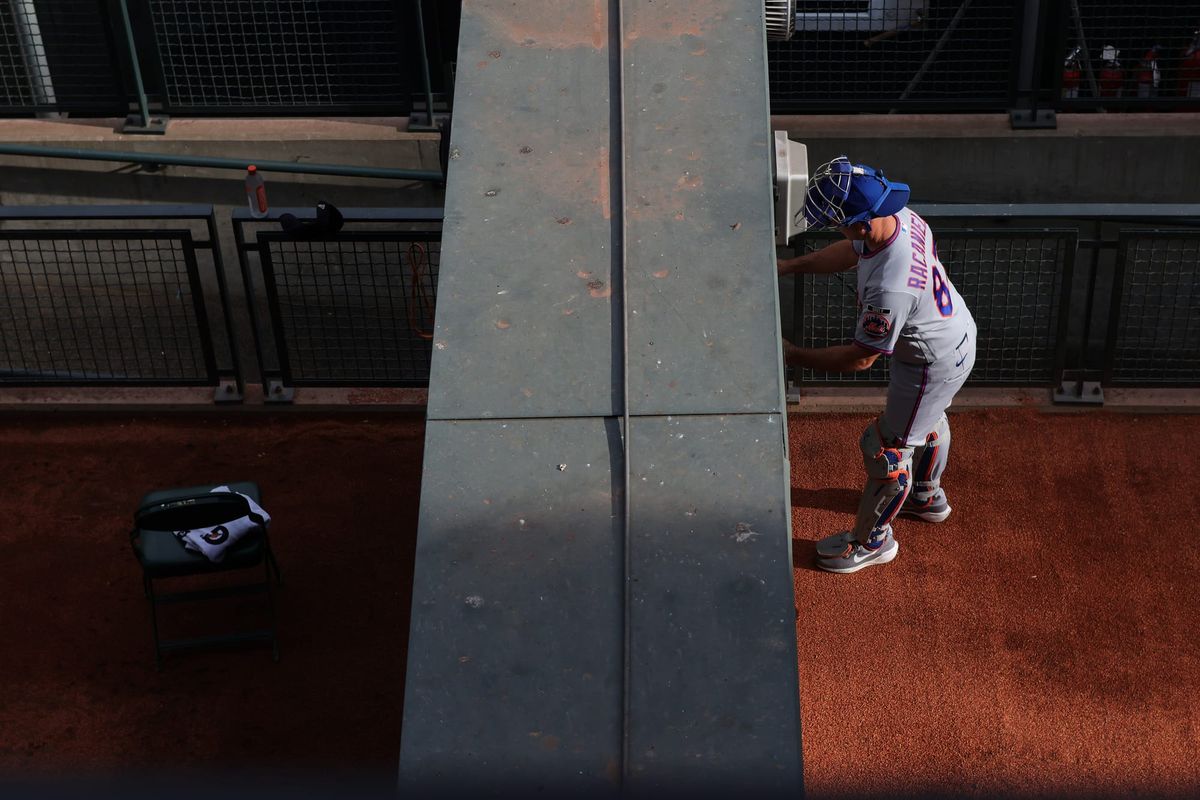 Bullpens at T-Mobile Park, split vertically by the wall between them. Left: Lone chair in the home bullpen. Right: Mets bullpen catcher Dave Racaniello in the visiting bullpen.