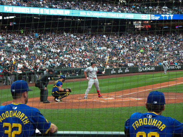 Minnesota Twins batter Ty France standing at home plate with catcher Cal Raleigh and the home plate umpire to the left, and a large crowd of fans at T-Mobile Park in the background.