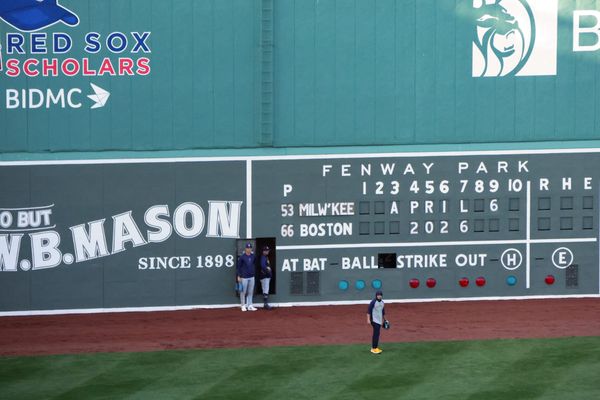 Three Milwaukee Brewers players/personnel stand in front of the scoreboard in the Green Monster at Fenway Park with its door open on April 6, 2026.