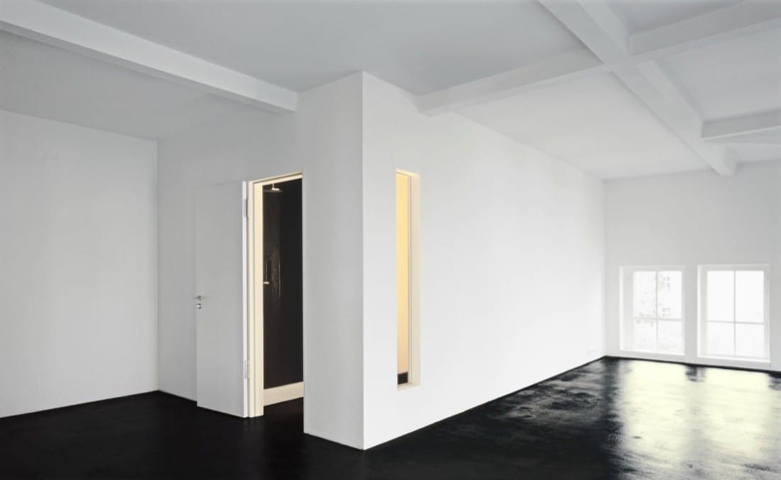 White interior room with black floor, narrow wall opening and soft daylight in the converted pumping station.
