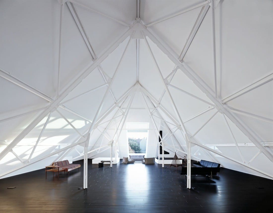 Bright attic workspace with white roof structure, black floor and desks beneath the pitched roof.