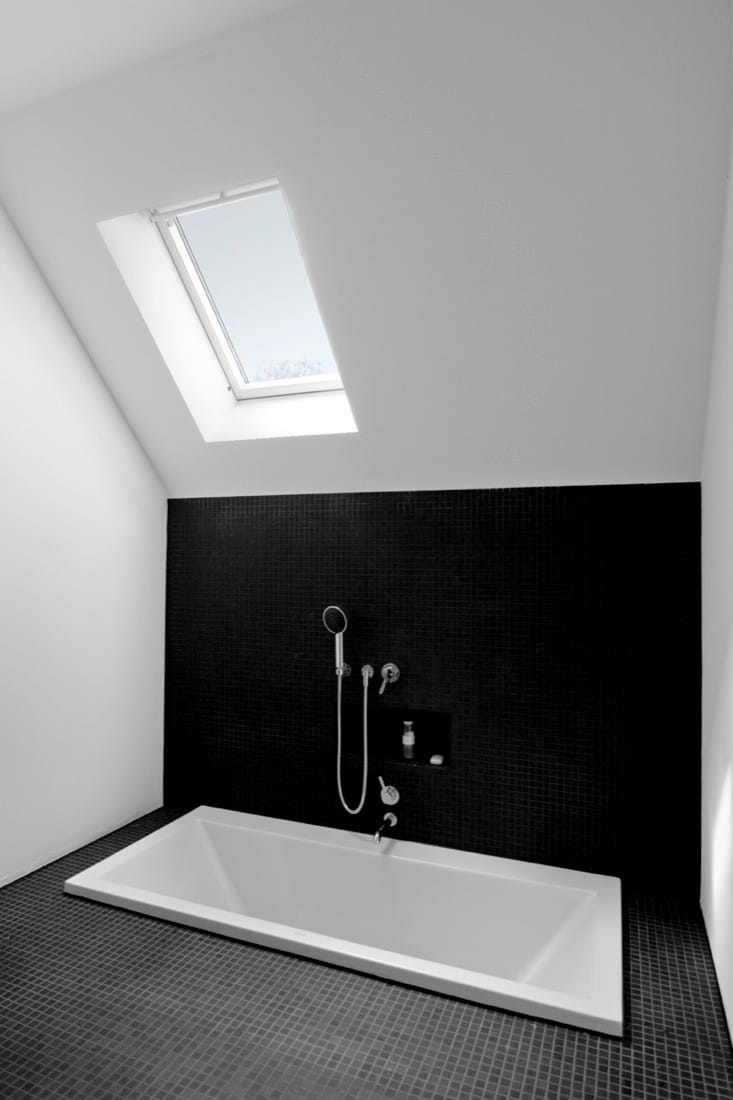 White bathroom with black walls, skylight and inset bathtub in the converted pumping station.