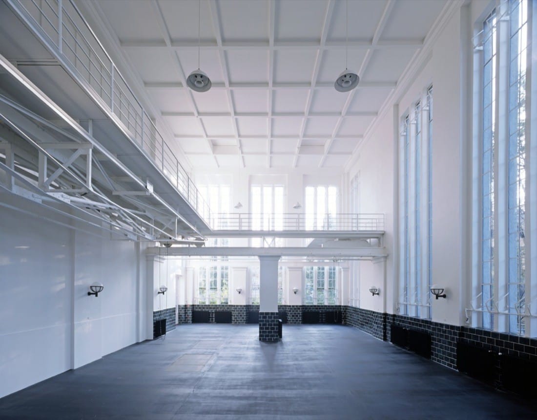 Open studio hall with white ceiling grid, black floor and tall windows in the former pumping station.