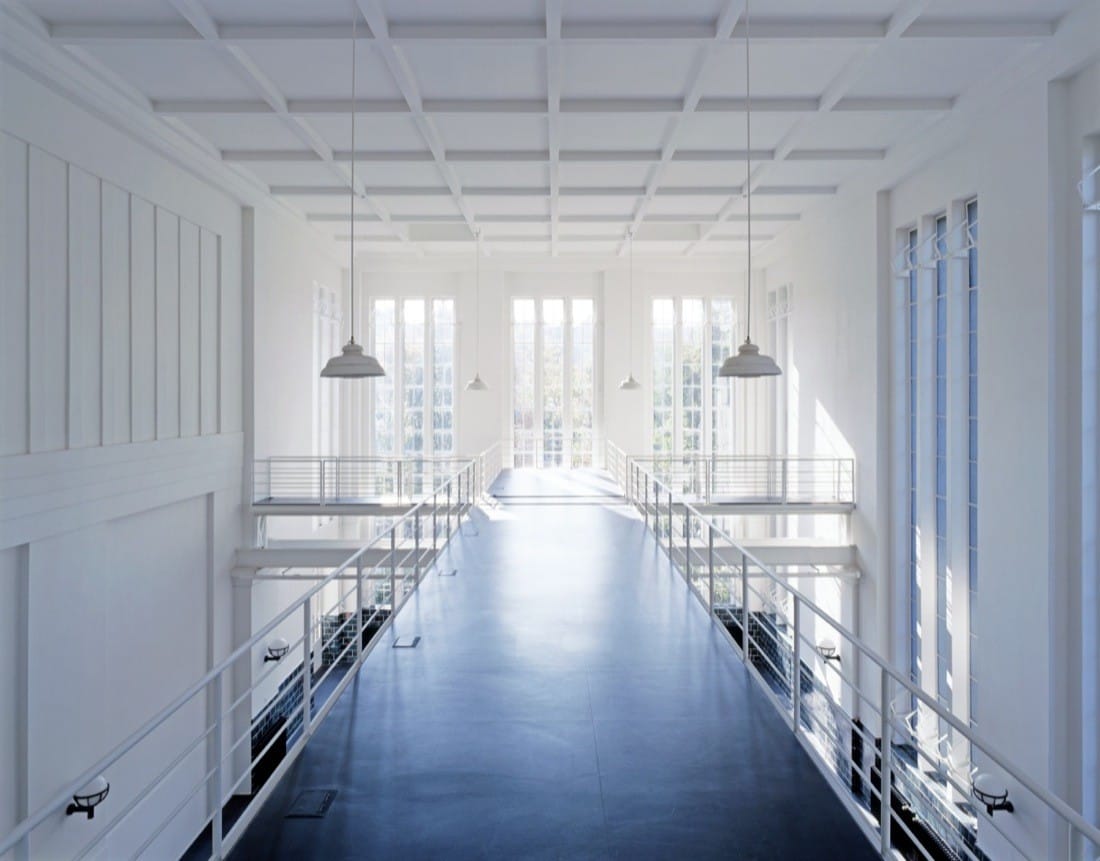 Bright upper walkway with white railings and windows overlooking the converted hall.