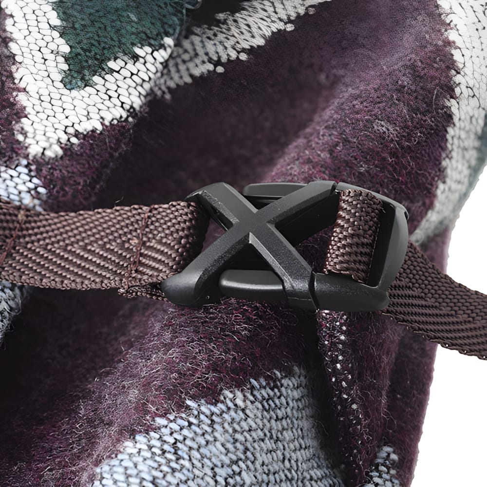 Close-up of black X-shaped side-release buckle on brown webbing strap against Kapital harlequin wool