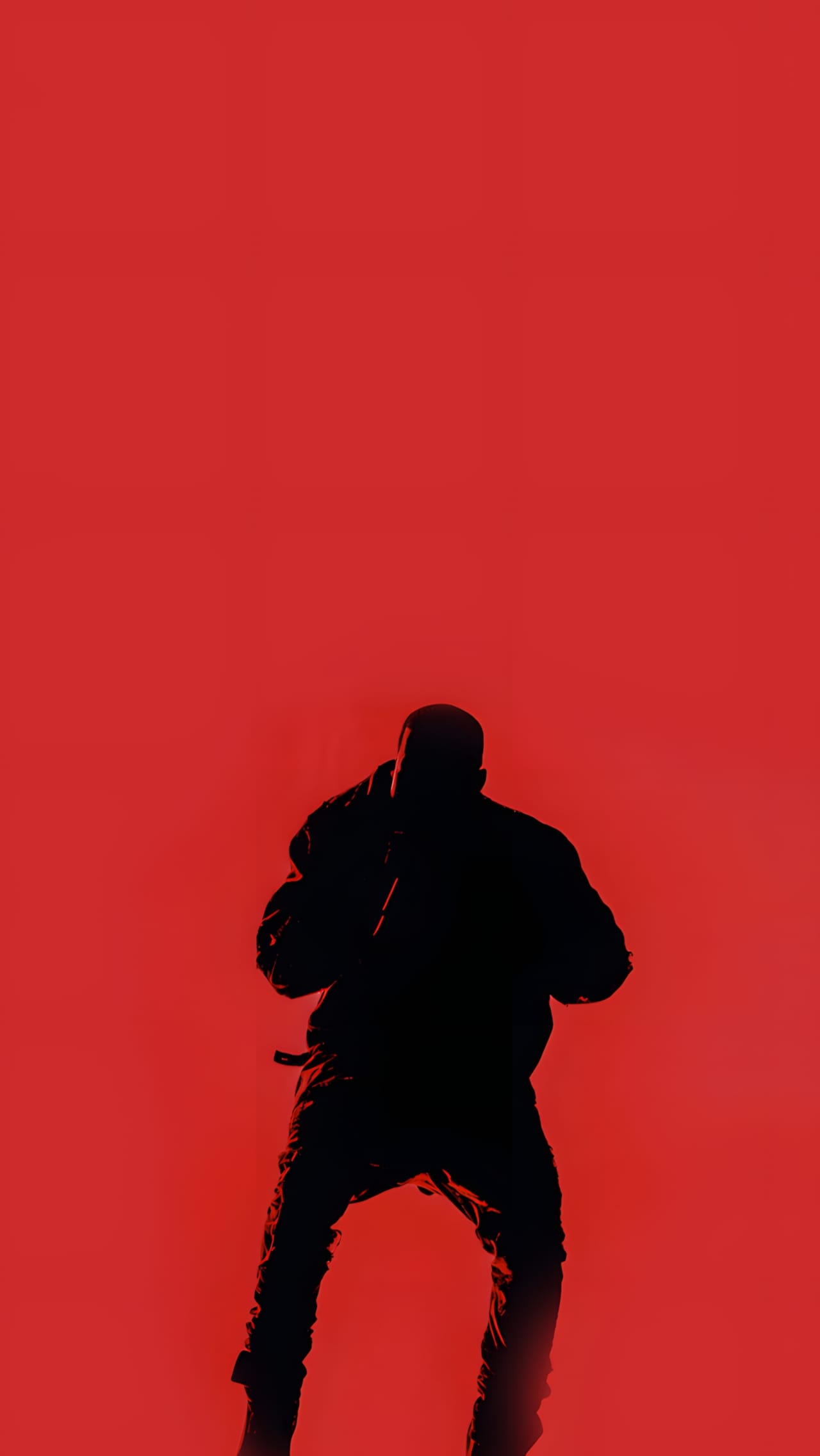 Full-length silhouette of Kanye West from behind on the Yeezus Tour stage, in deep red light, in a long structured Maison Martin Margiela coat.