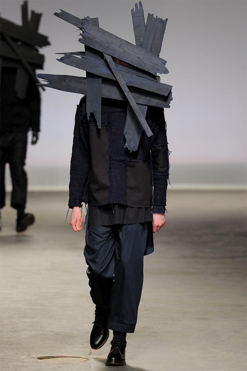 Craig Green FW2013 MAN look 2 — black-and-white patchwork layered coat with wide-leg trousers and splintered timber headpiece