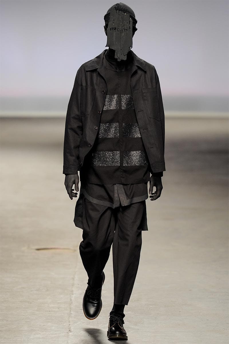 Craig Green FW2013 MAN look 14 — tonal black layered drapery with waxed-cotton panels and sculptural timber headpiece