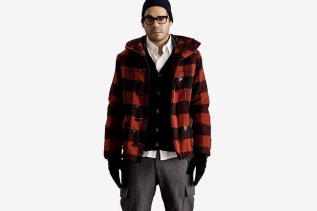 Model in a red and black buffalo-plaid Stussy jacket layered over a cardigan and white shirt.