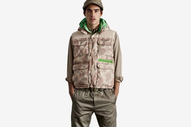Model in a beige camouflage Stussy puffer vest with bright green zip pocket and hood.