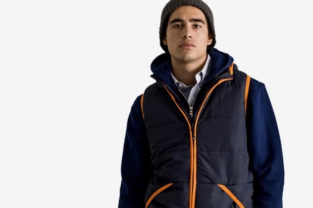Model in a navy Stussy Japan padded vest with orange piping over a blue hooded jacket.