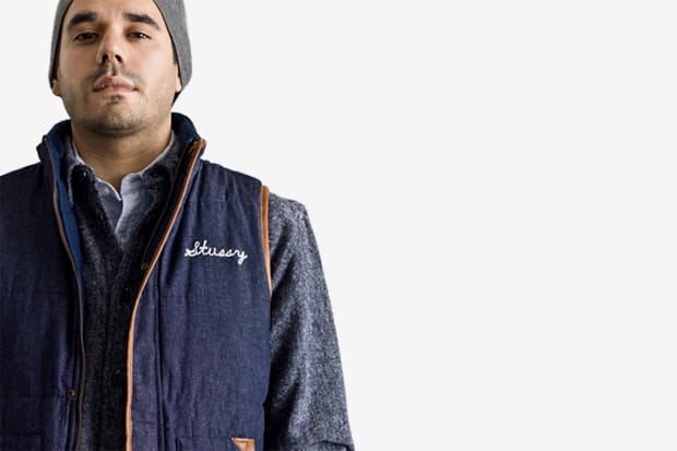 Model in a navy Stussy Japan padded vest with orange piping over grey knit layers.