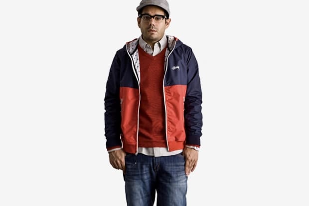 Model in a navy and red Stussy Japan color-block hooded jacket layered over a red sweater.