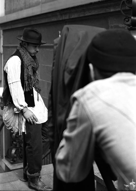 Model in a brimmed hat, scarf, vest and long shirt posing during the Times Square Redux shoot.