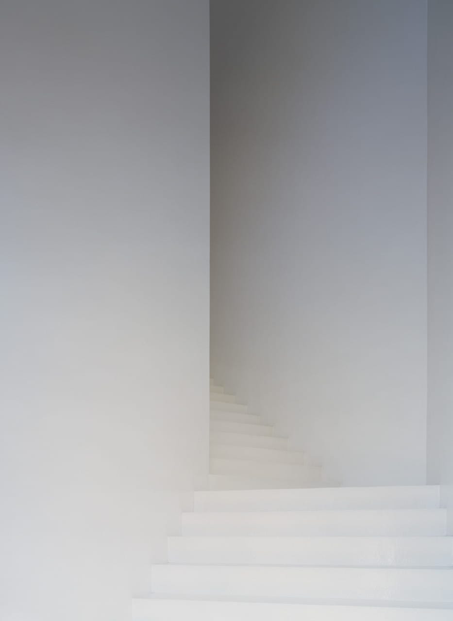 Minimal white staircase rising through a narrow, softly lit interior at Casa dos Cubos.