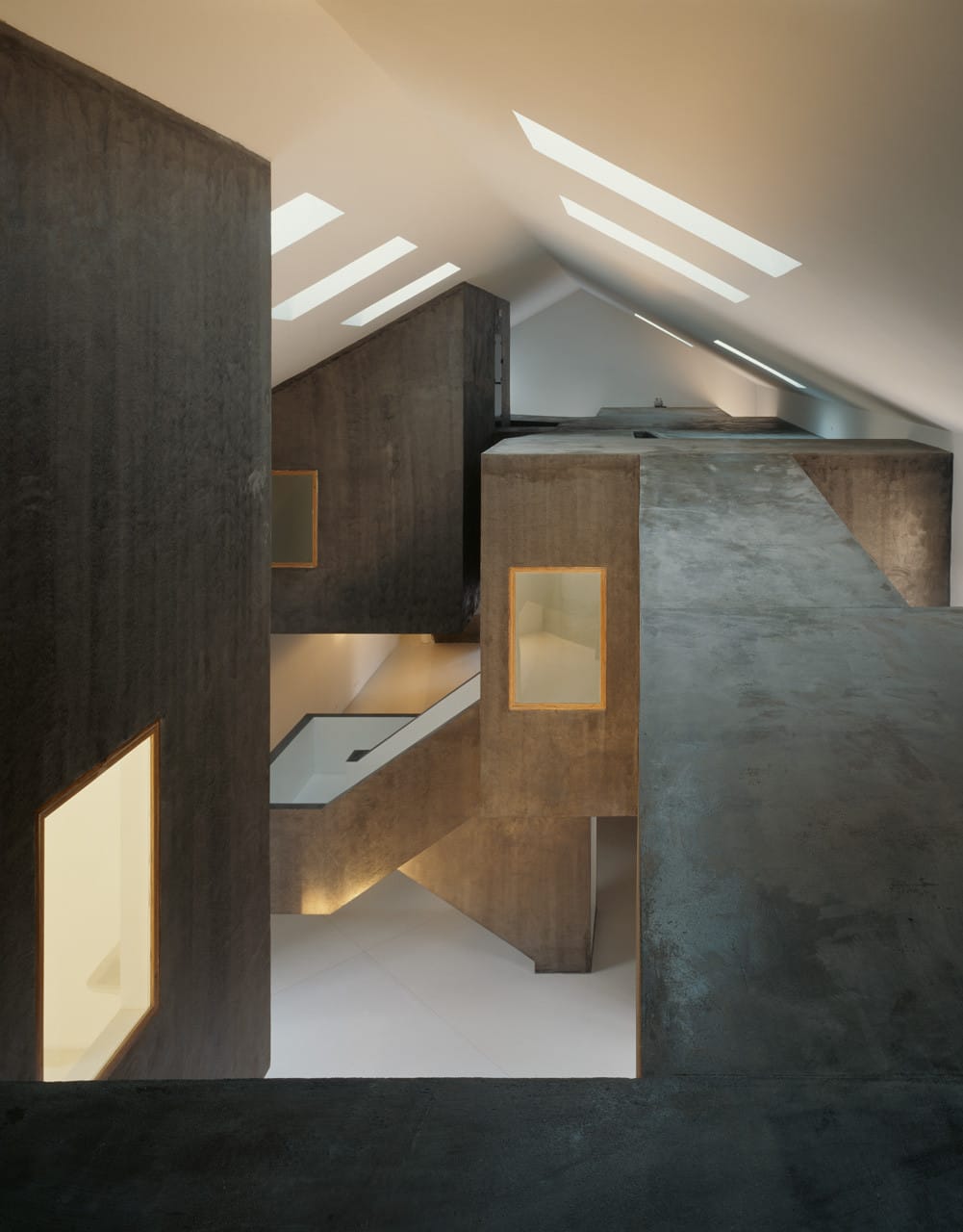 Upper-level view across dark angular room volumes and long rooflights inside Casa dos Cubos.