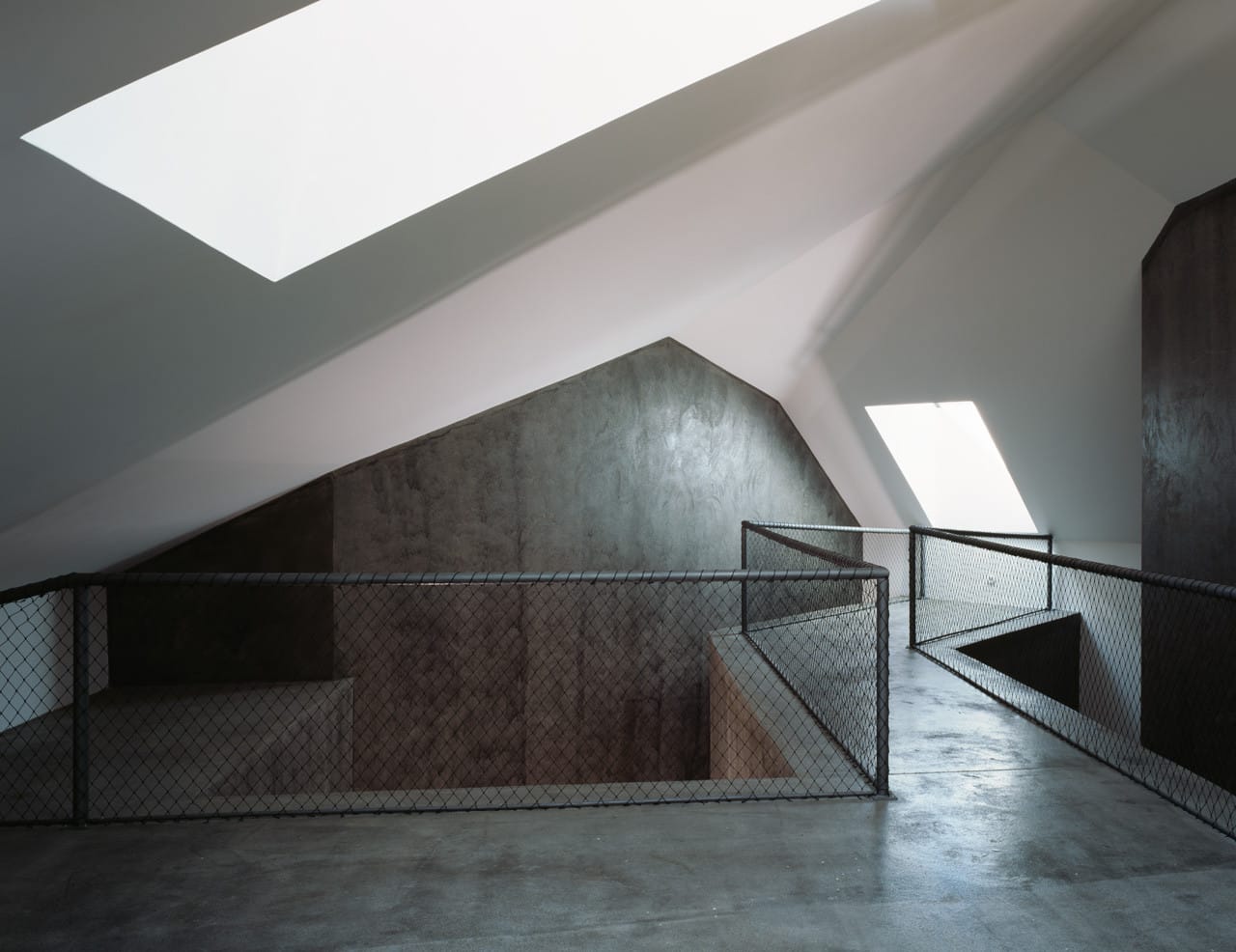 Upper gallery with mesh railings, angular dark volumes and rooflights inside Casa dos Cubos.