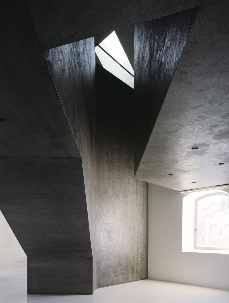 Vertical dark concrete structure opening toward a skylit void inside Casa dos Cubos.