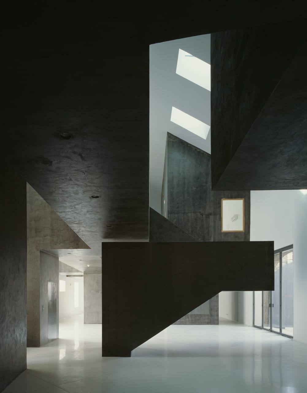 Wide Casa dos Cubos interior with a dark cantilevered stair volume, skylights and glass doors.