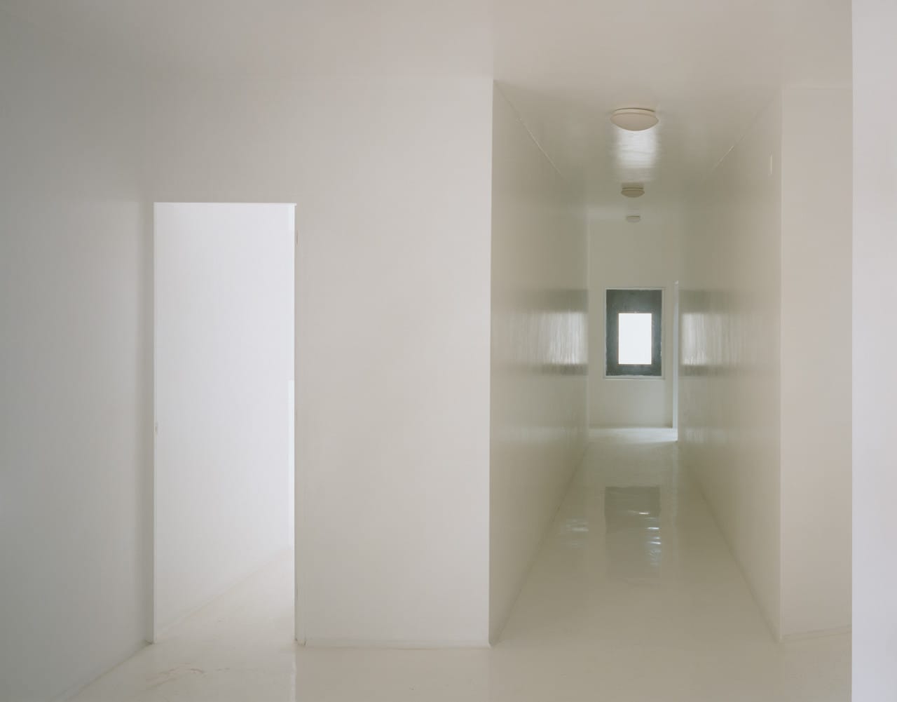 Glossy white corridor and doorways leading to a dark-framed window at Casa dos Cubos.
