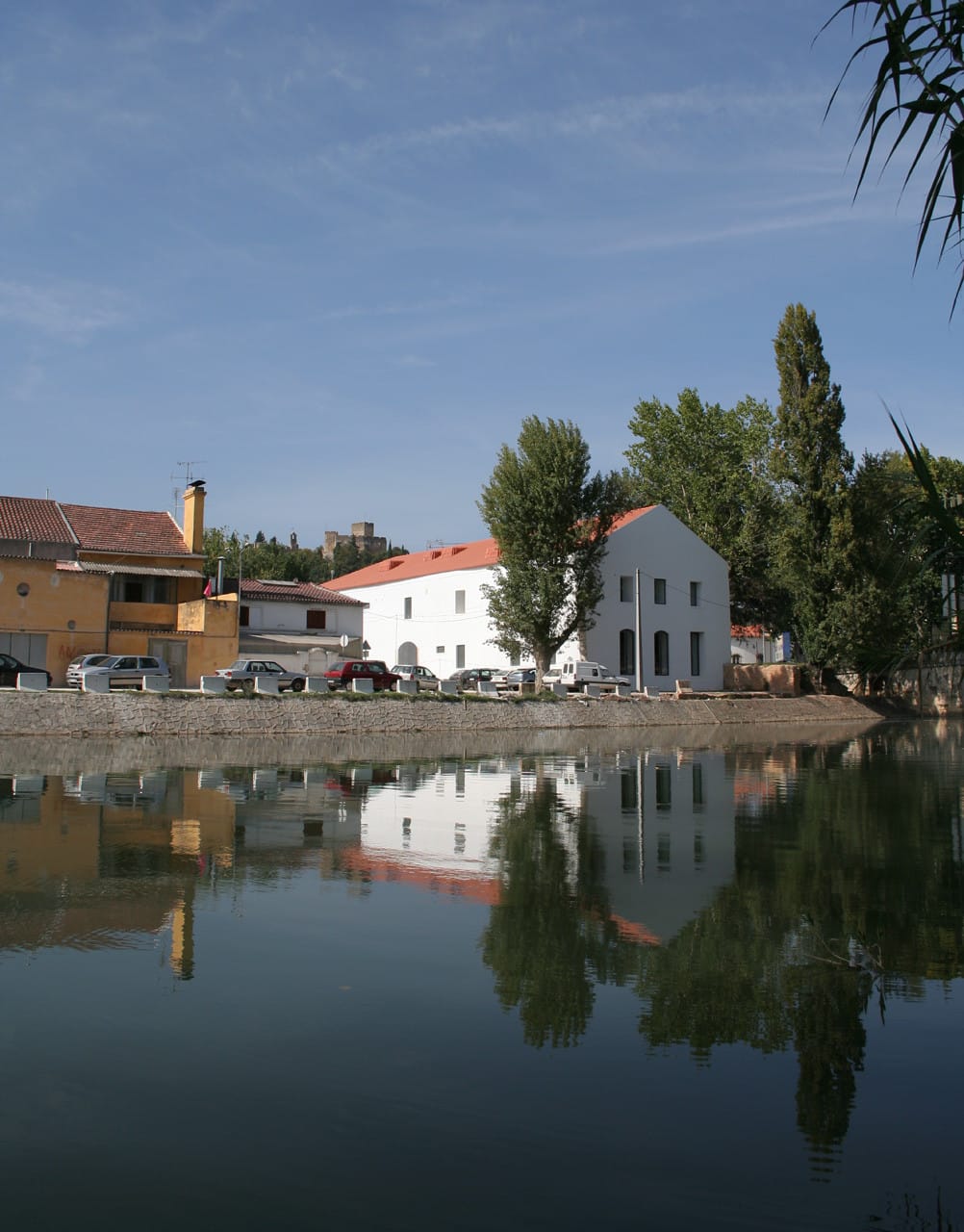 White riverside exterior of Casa dos Cubos in Tomar reflected in the water.