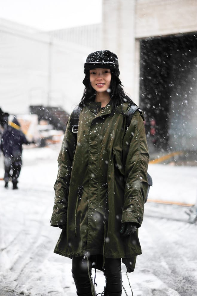 Portrait of Xiao Wen Ju in an olive parka and black earflap cap during snowfall in New York.