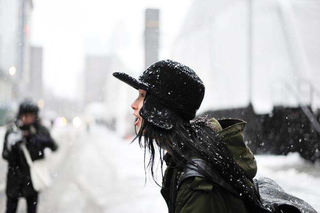 Side profile of Xiao Wen Ju in a snow-covered black cap, olive hooded parka and black backpack.