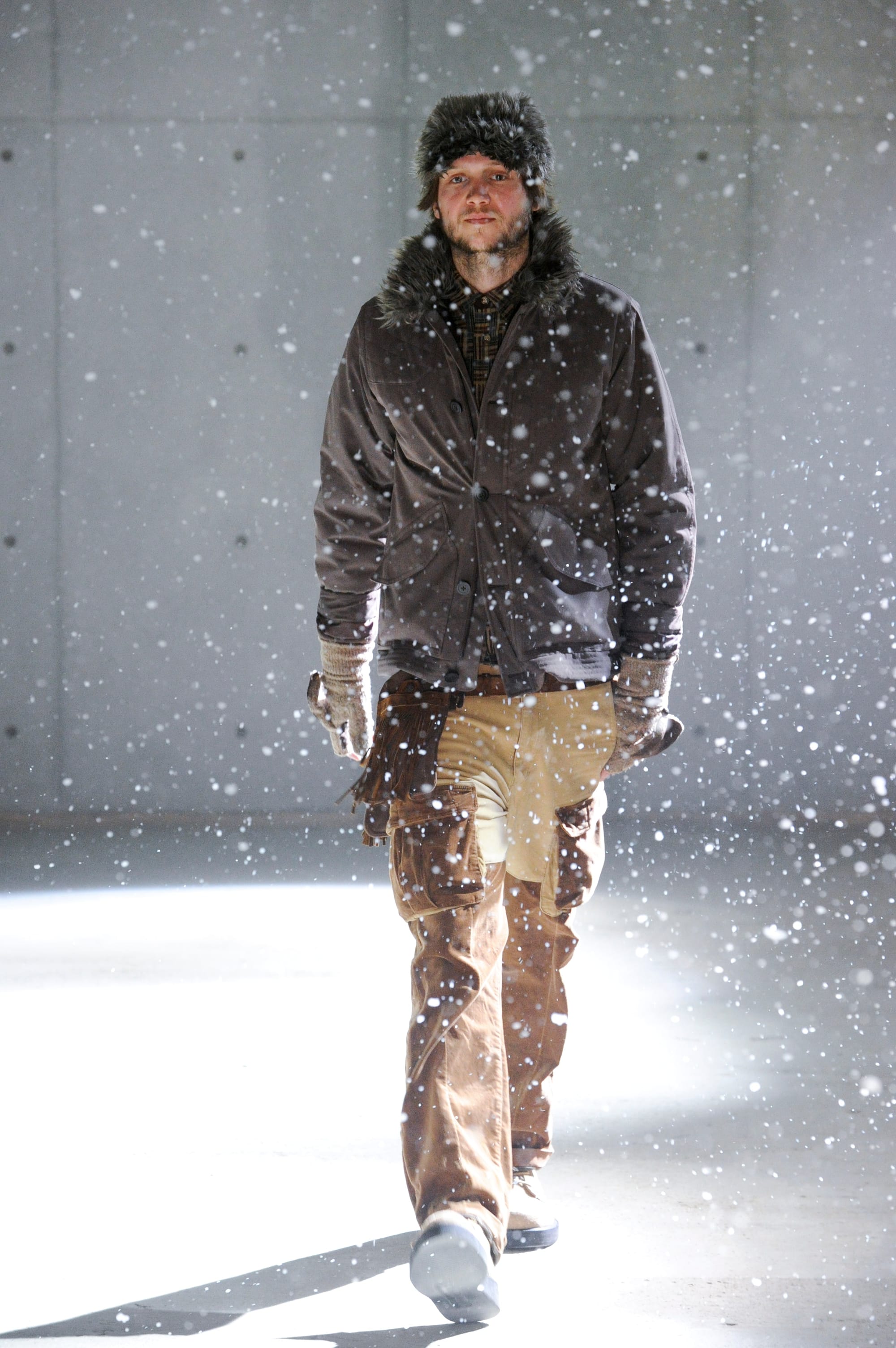 White Mountaineering Wilderness Outfitters look 21: plaid jacket over a black multi-pocket hunting vest and grey trousers.