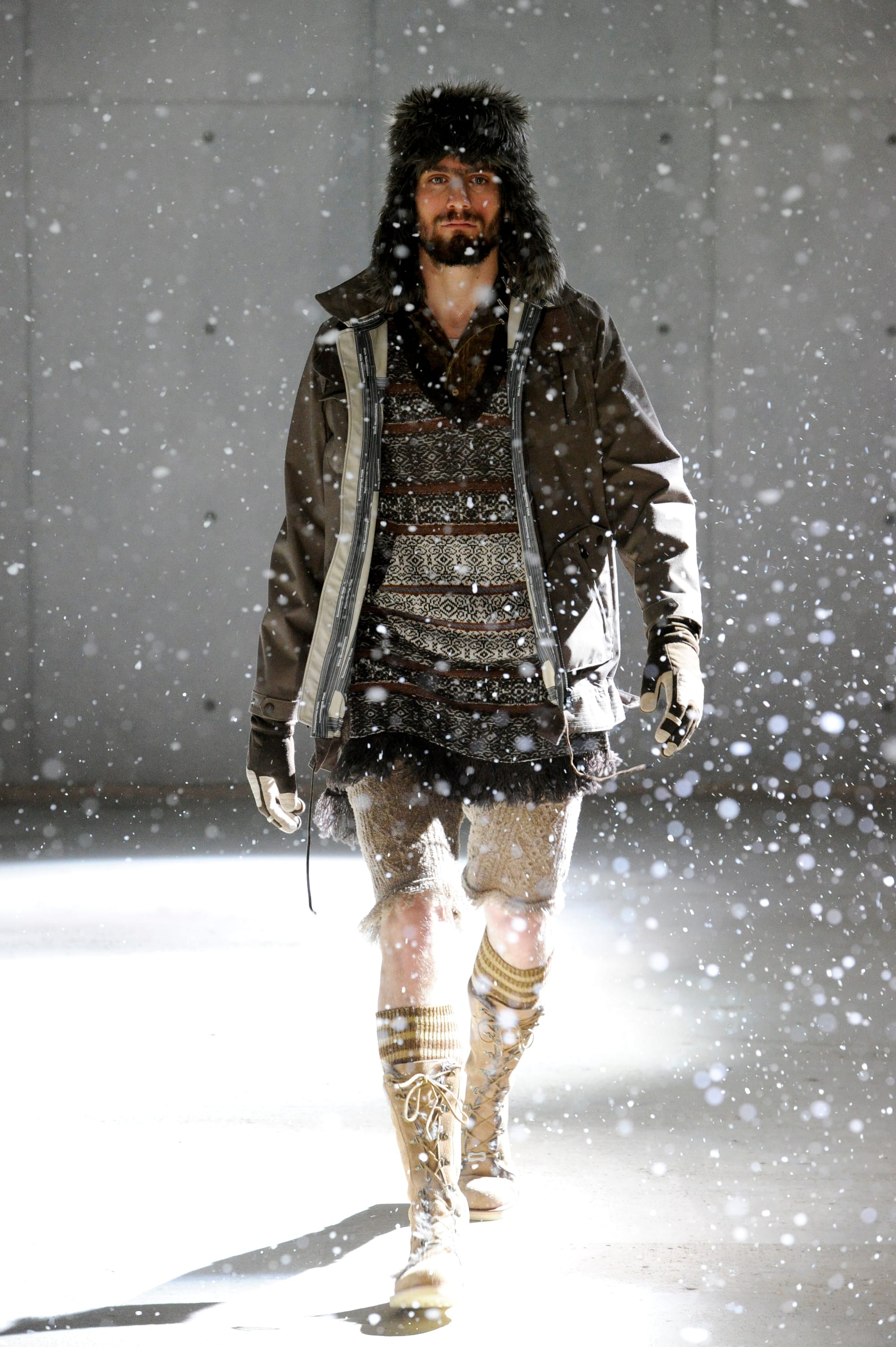 White Mountaineering Wilderness Outfitters look 30: brown technical shell over a jacquard knit with fur hat and cropped shorts.