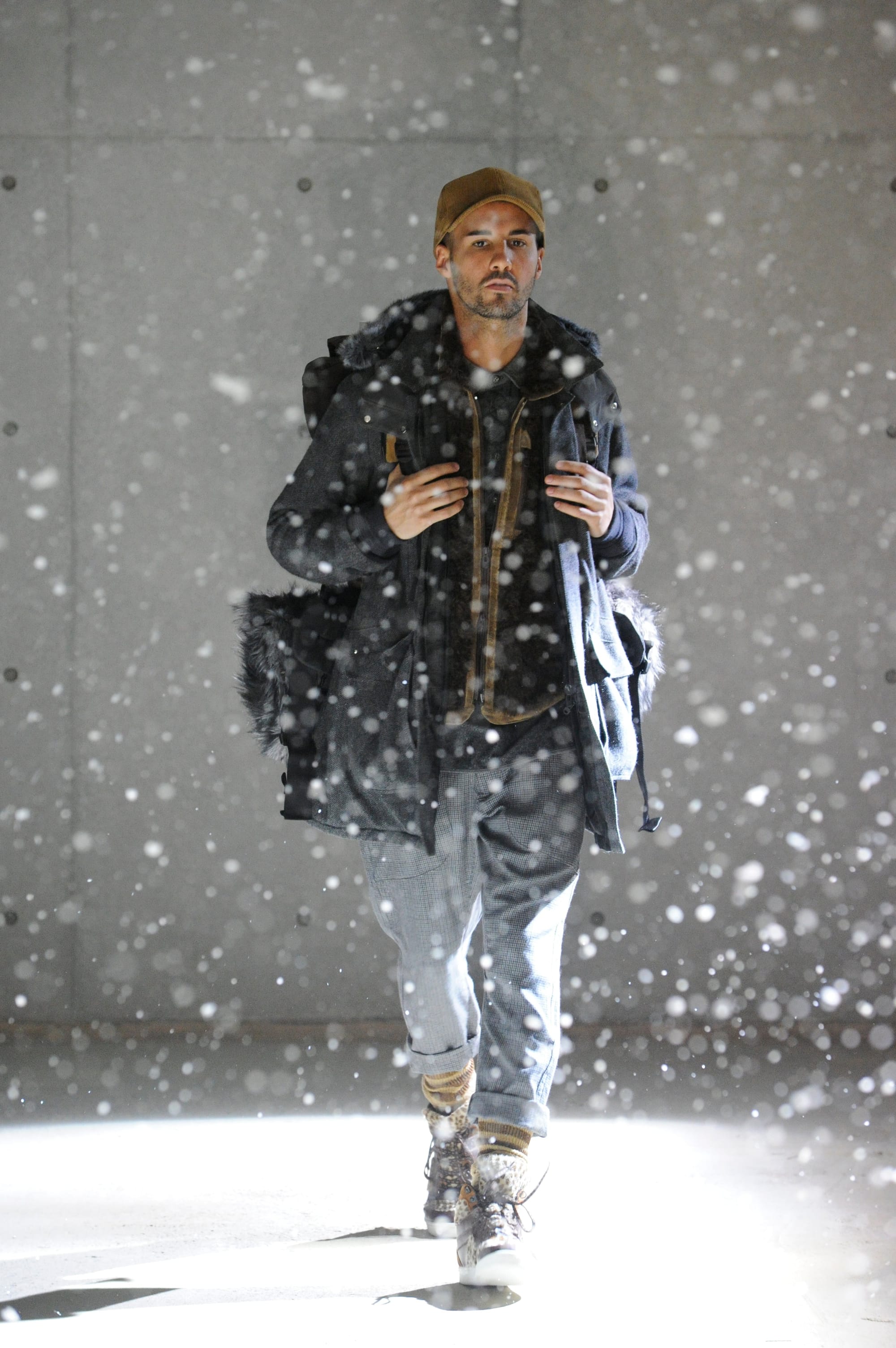 White Mountaineering Wilderness Outfitters look 31: black fur-trimmed backpack coat, grey checked trousers and patterned boots.