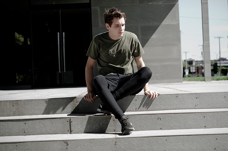 Model in an olive DDWD T-shirt seated on concrete steps for Deadwood Fall/Winter 2012.