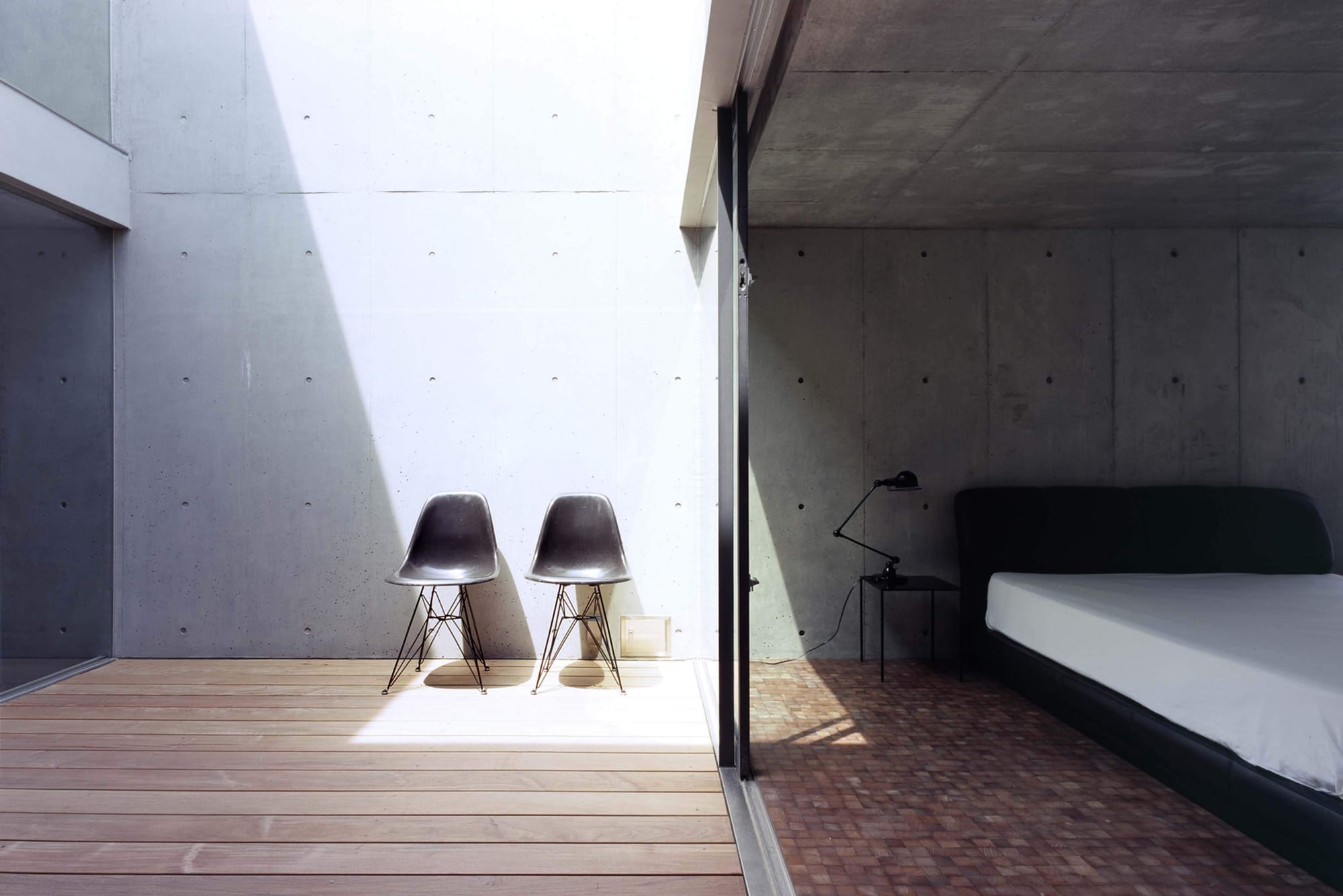 Sunlit bedroom and courtyard inside 2COURTS HOUSE, with two Eames shell chairs against exposed concrete.