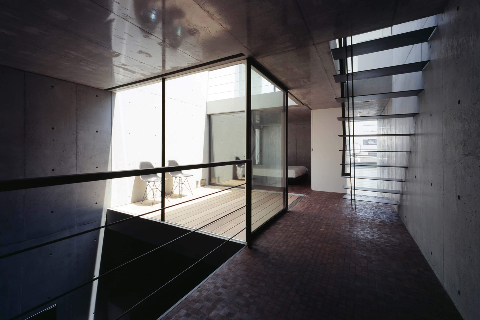 Upper-level walkway and courtyard framed by exposed concrete and black steel inside 2COURTS HOUSE.