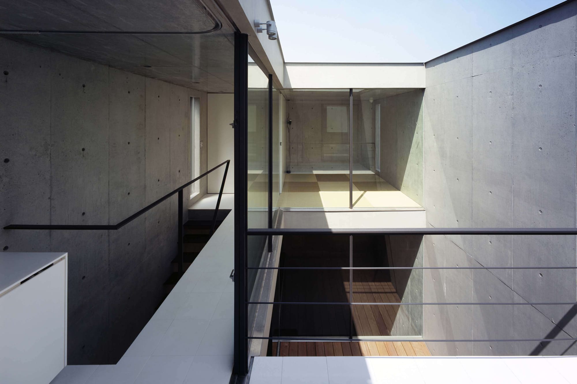 Cascading concrete lightwell viewed across an upper-level railing in 2COURTS HOUSE.