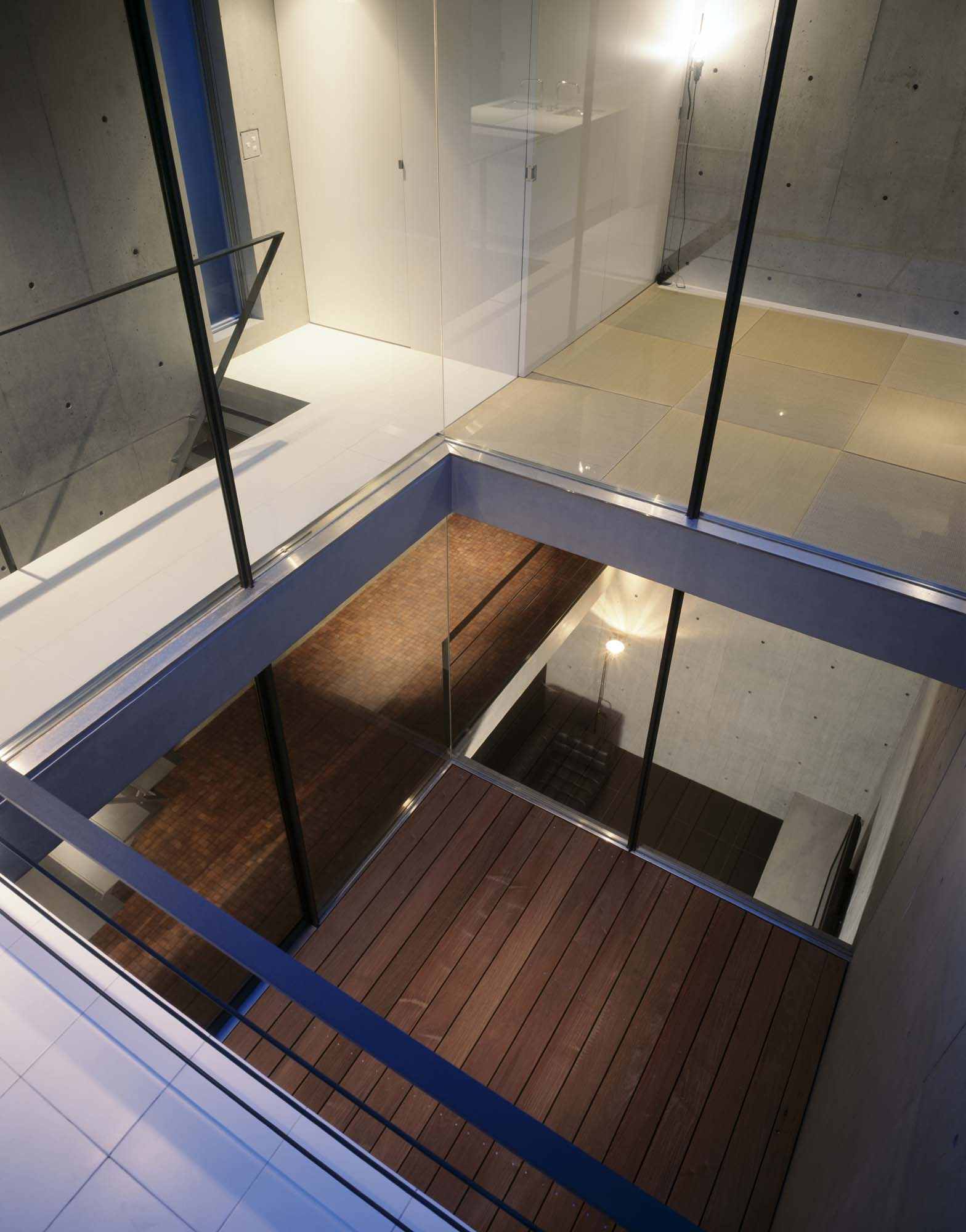 Glass floor, steel framing and stacked courtyards viewed from above inside 2COURTS HOUSE.