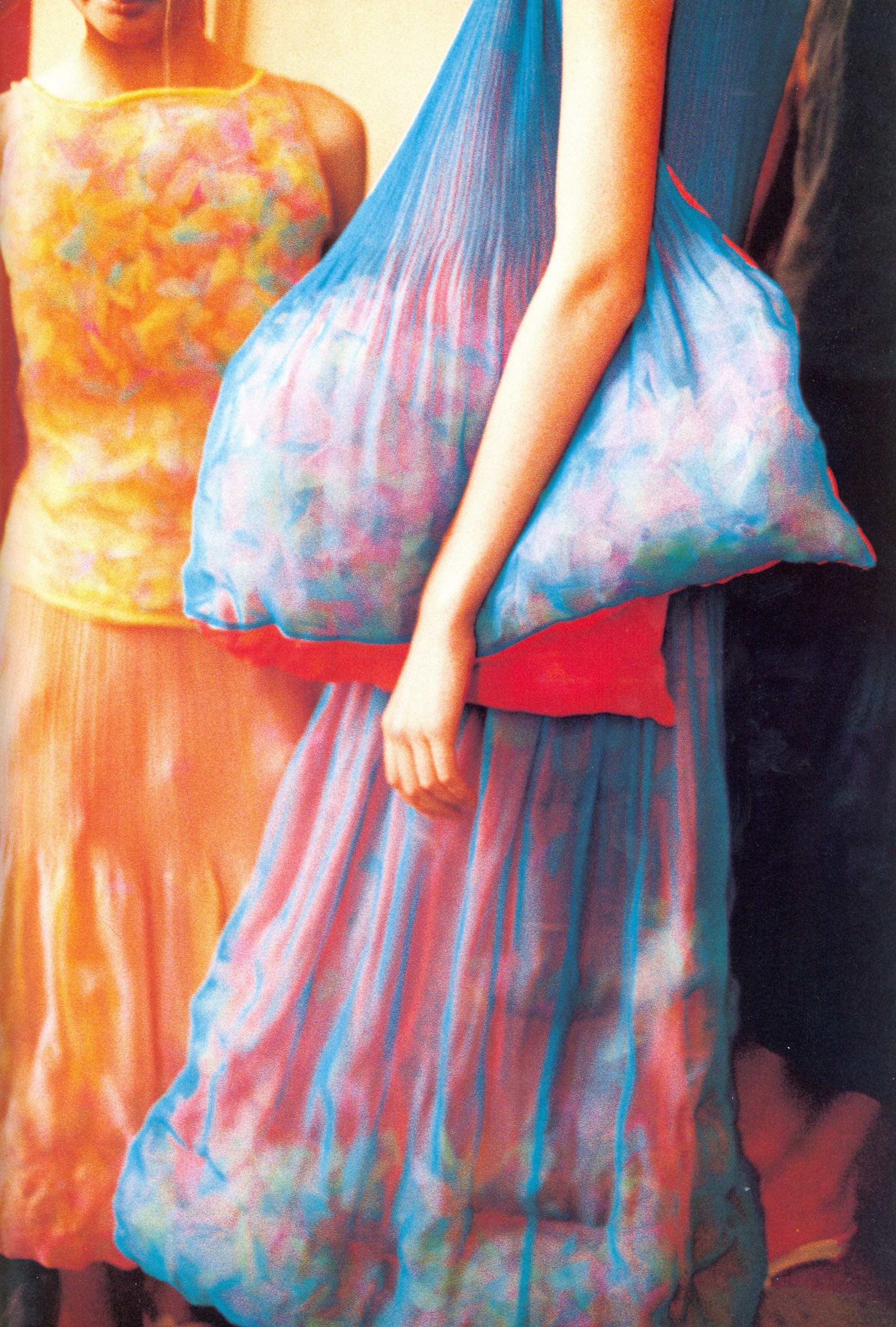 Cropped view of a blue and pink pleated dress with rounded padded forms beside an orange patterned outfit.