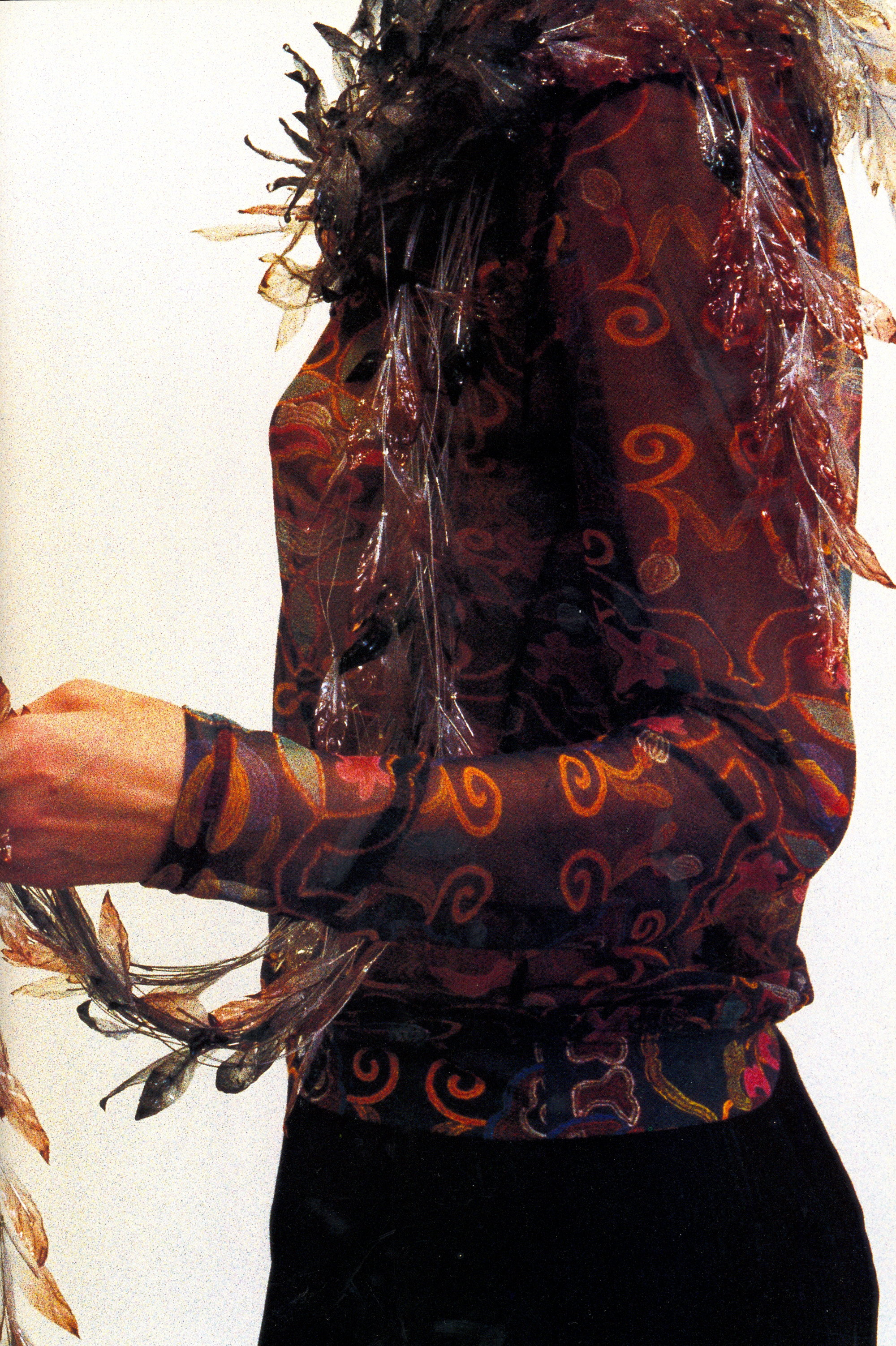 Side view of a sheer dark top with orange scroll patterns and transparent fringe.