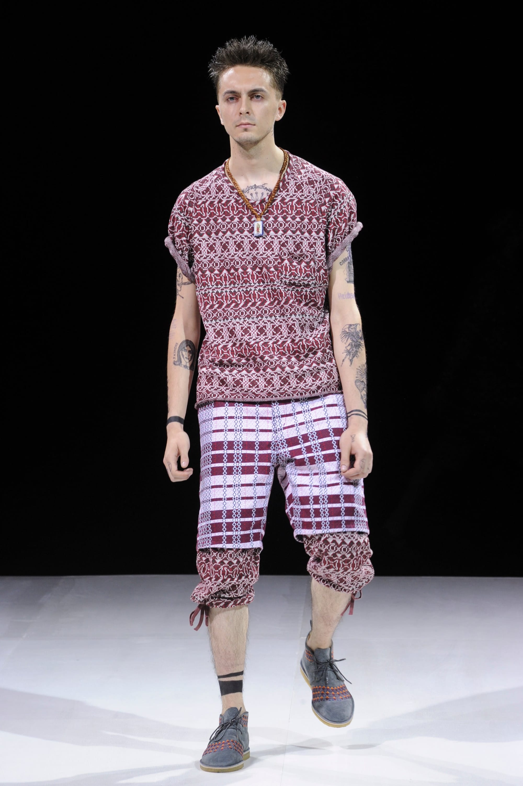 Model in a red patterned knit top and red-and-white plaid cropped trousers.