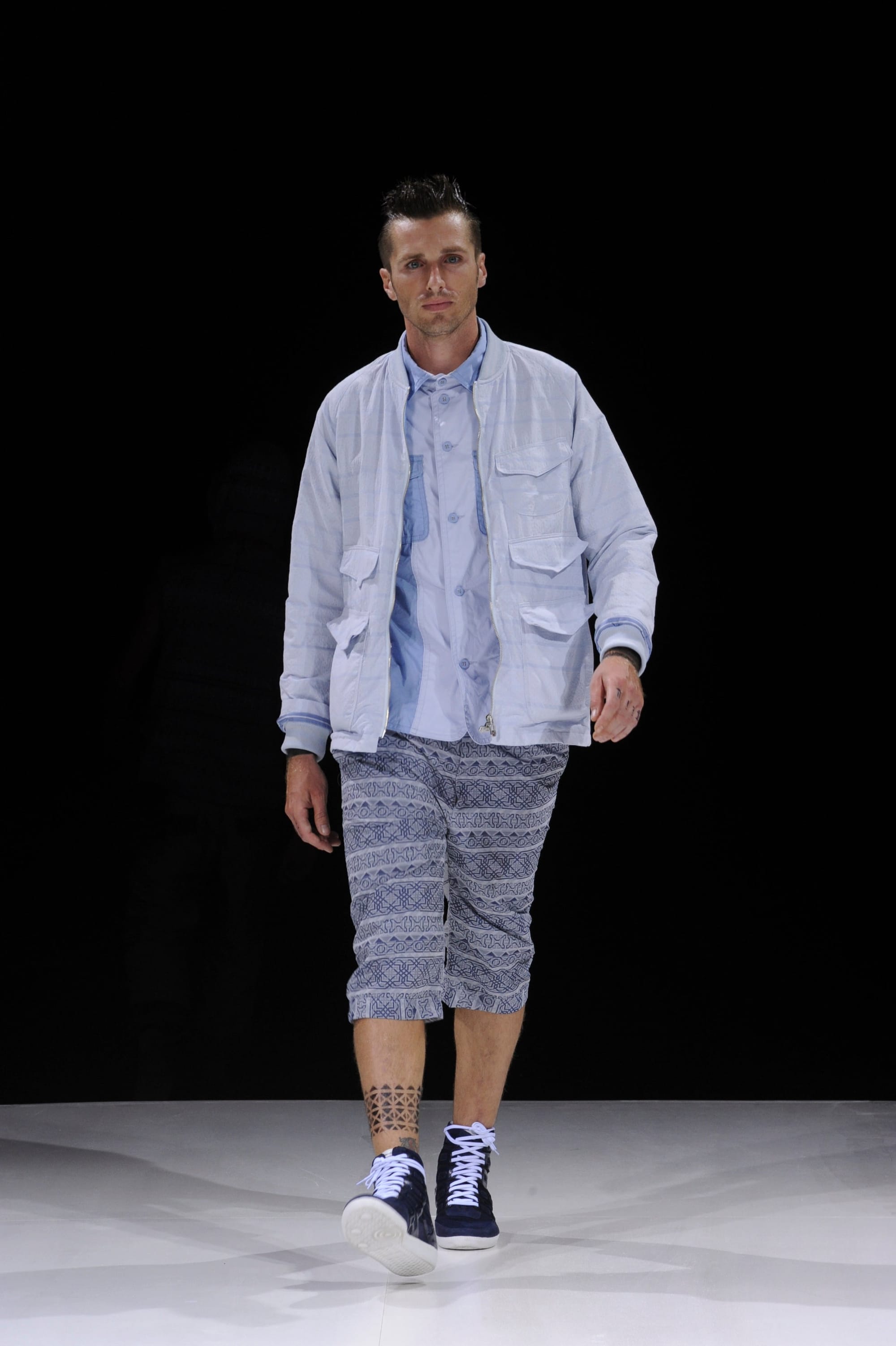 Model in a pale blue utility jacket and blue patterned knee-length shorts.