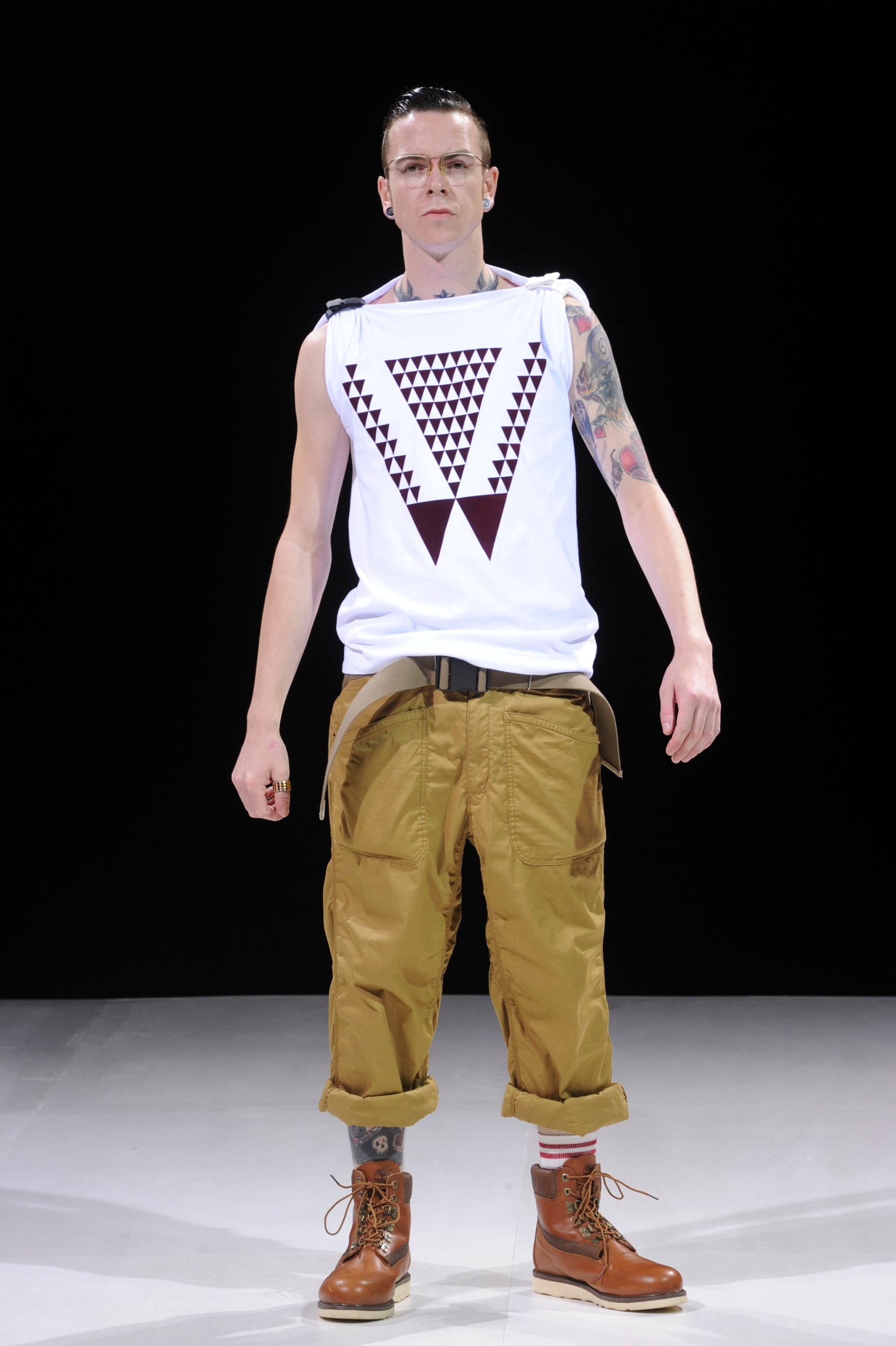 Model in a white triangle-print sleeveless top, tan cropped cargo trousers, and brown boots.