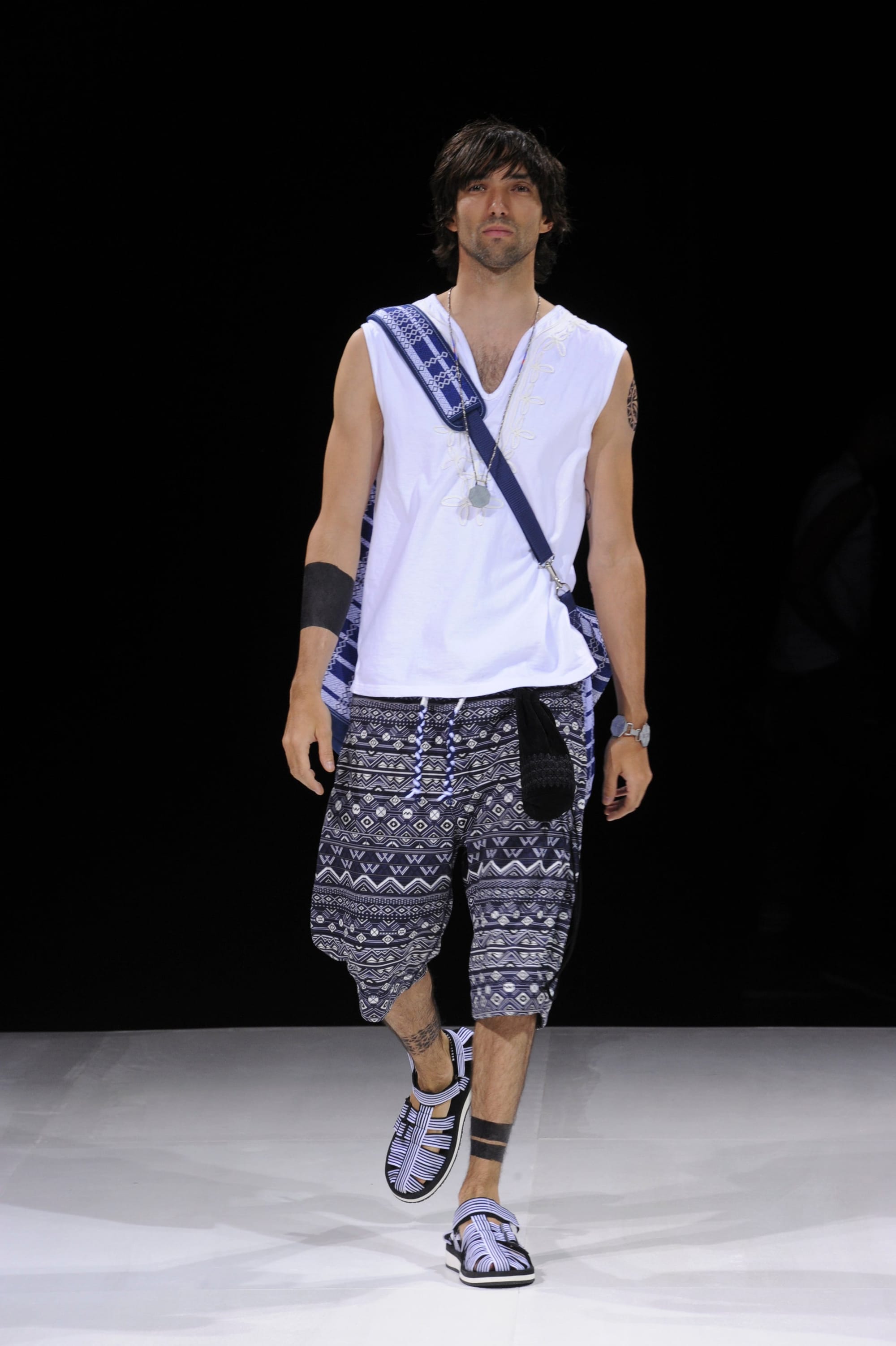 Model in a white sleeveless top, navy patterned knee-length trousers, and a crossbody strap.