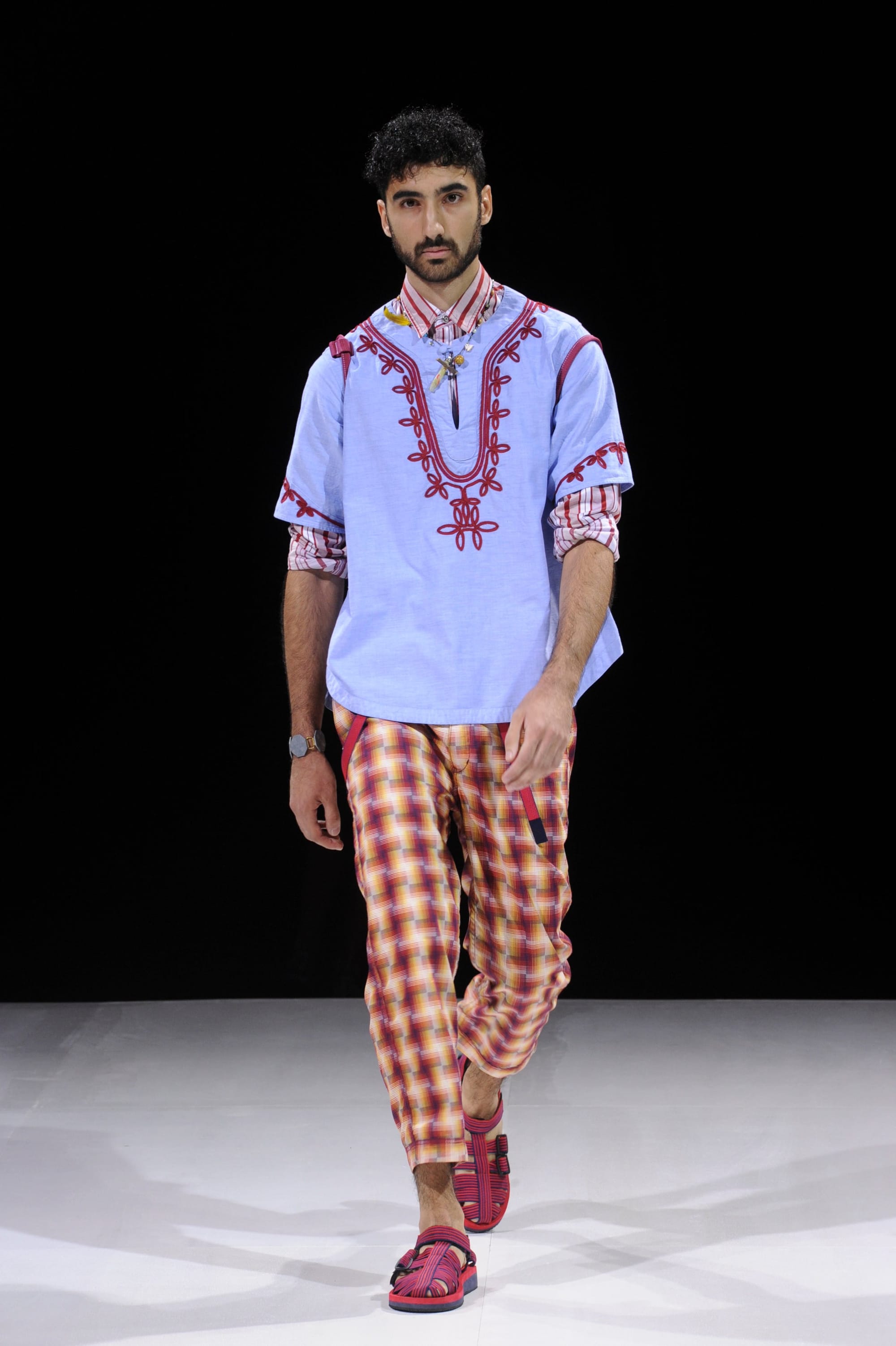 Model in a pale blue embroidered tunic over orange plaid cropped trousers.