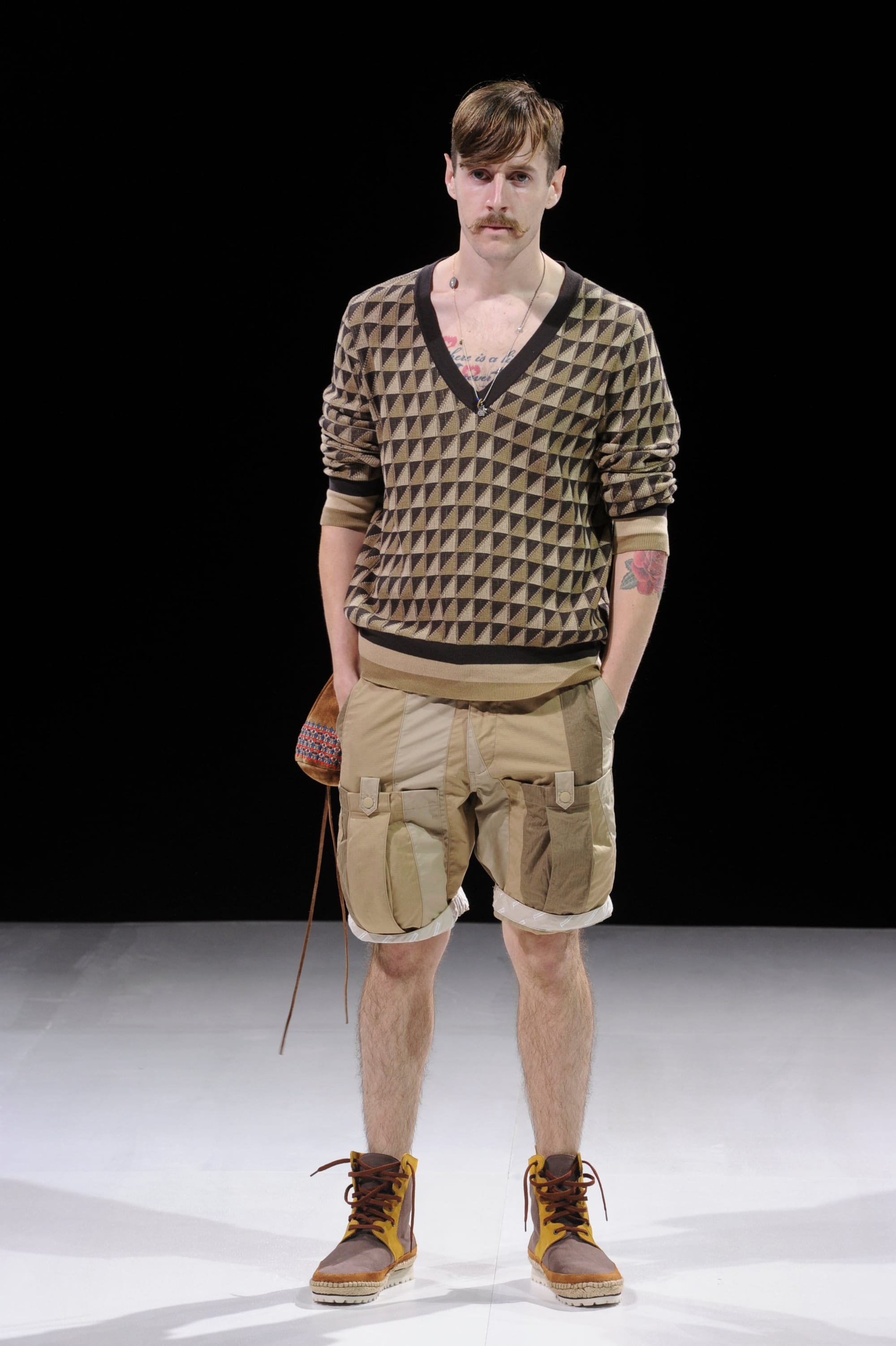Model in a brown triangle-pattern knit top and tan cargo shorts.