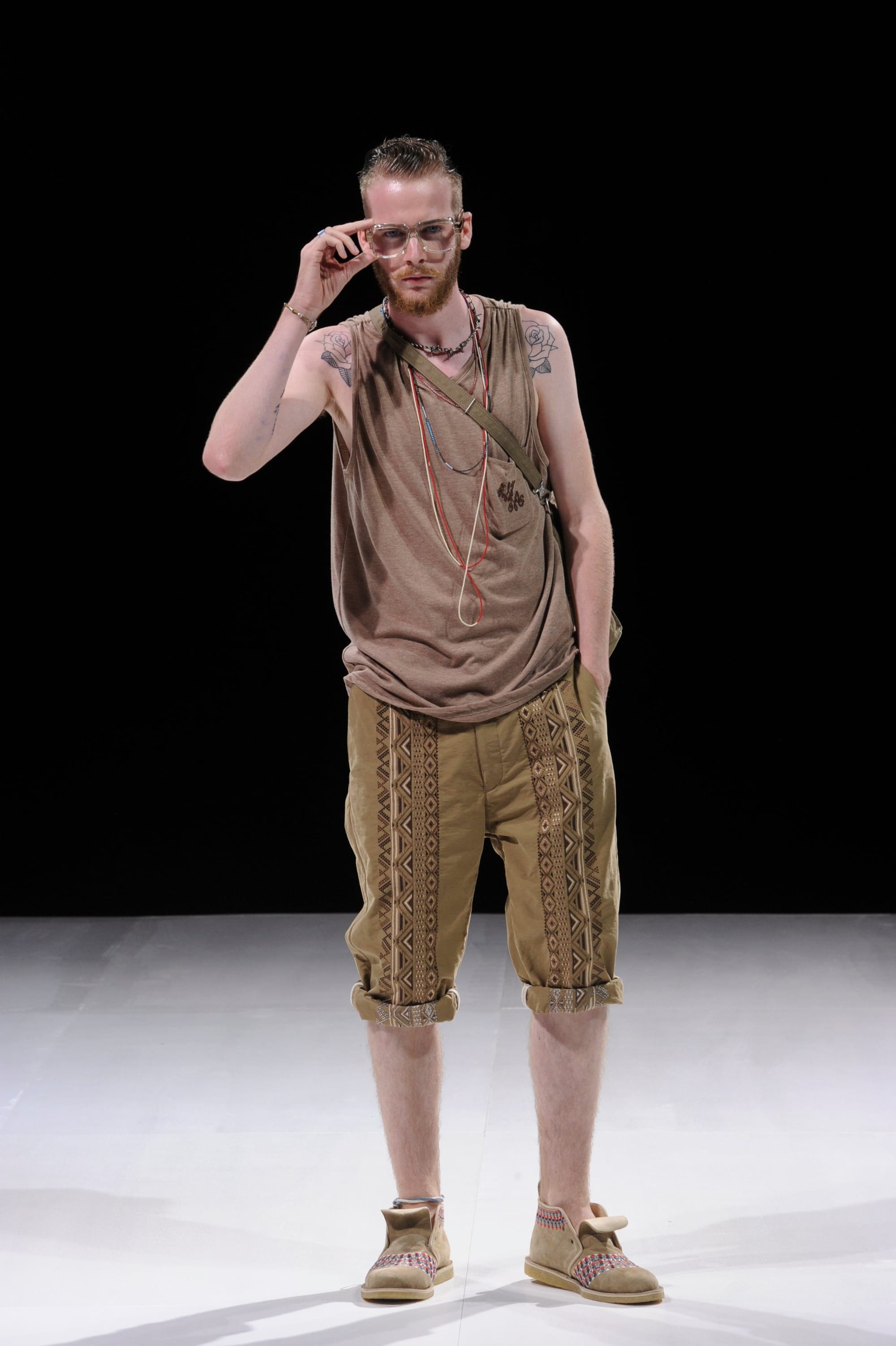 Model in a taupe sleeveless draped top and brown embroidered knee-length shorts.
