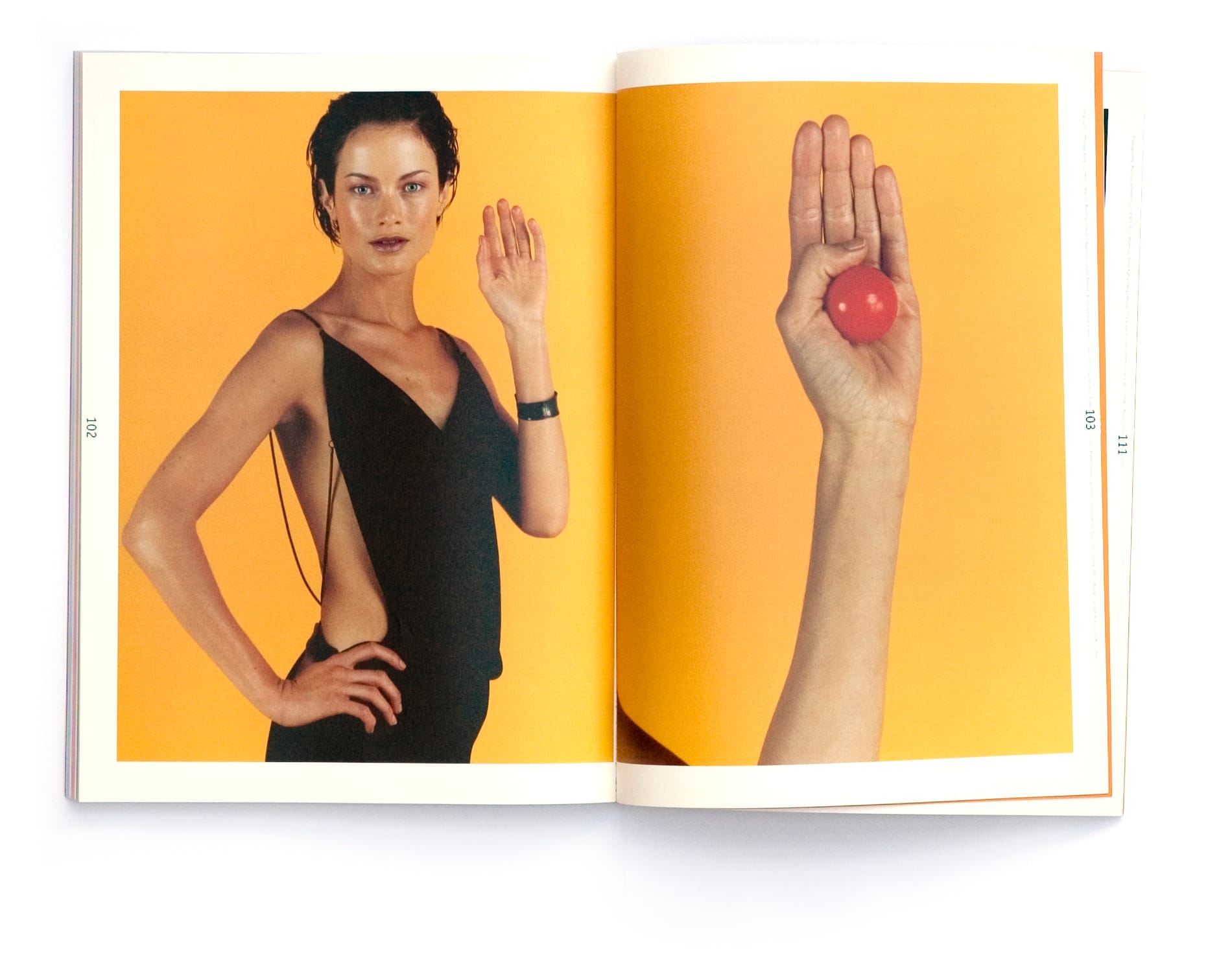 Woman in an asymmetric black dress paired with an upright hand holding a glossy red sphere on orange.