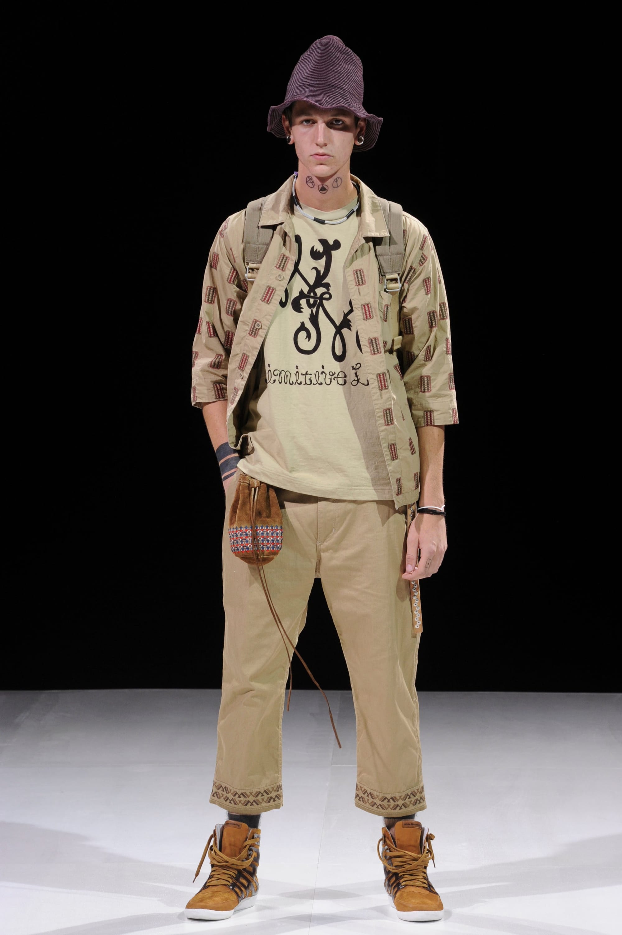 Model in a beige printed jacket and cropped trousers with a purple knit cap.