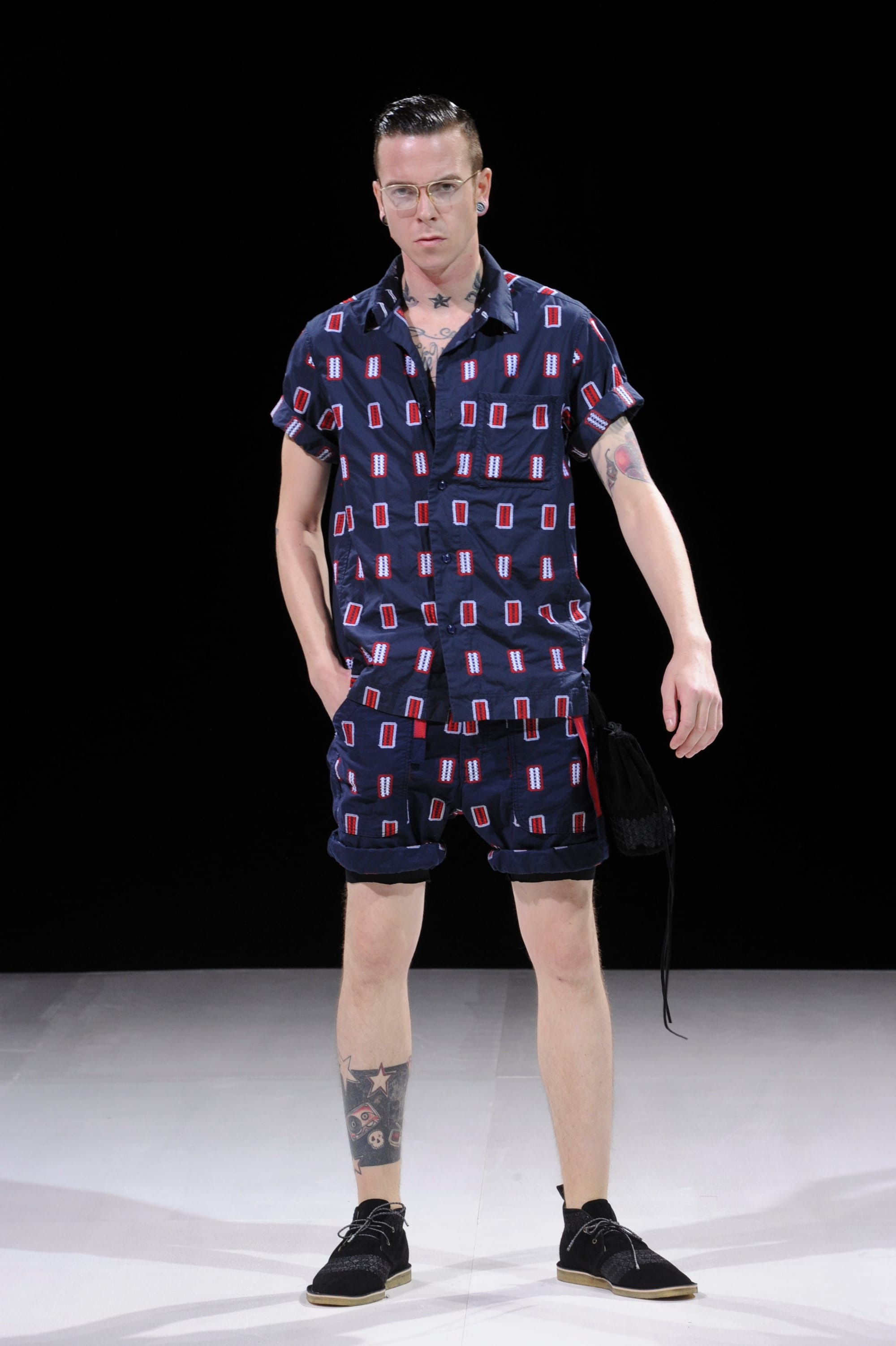 Model in a navy short-sleeve shirt and matching shorts with red-and-white rectangular motifs.