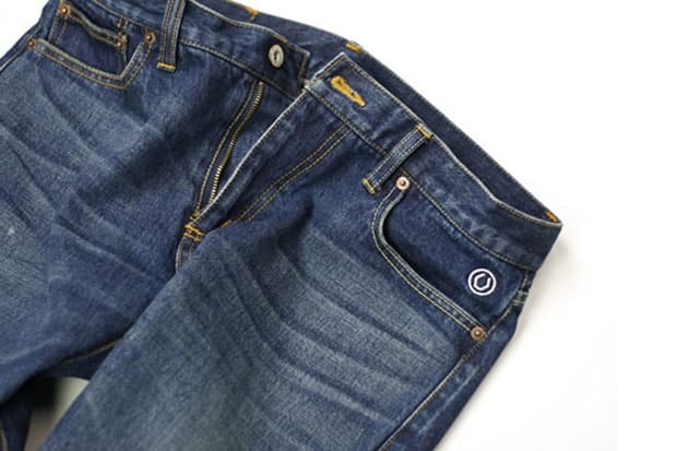 UNTOLD washed indigo jeans with yellow contrast stitching and an embroidered circular U logo on the front pocket.