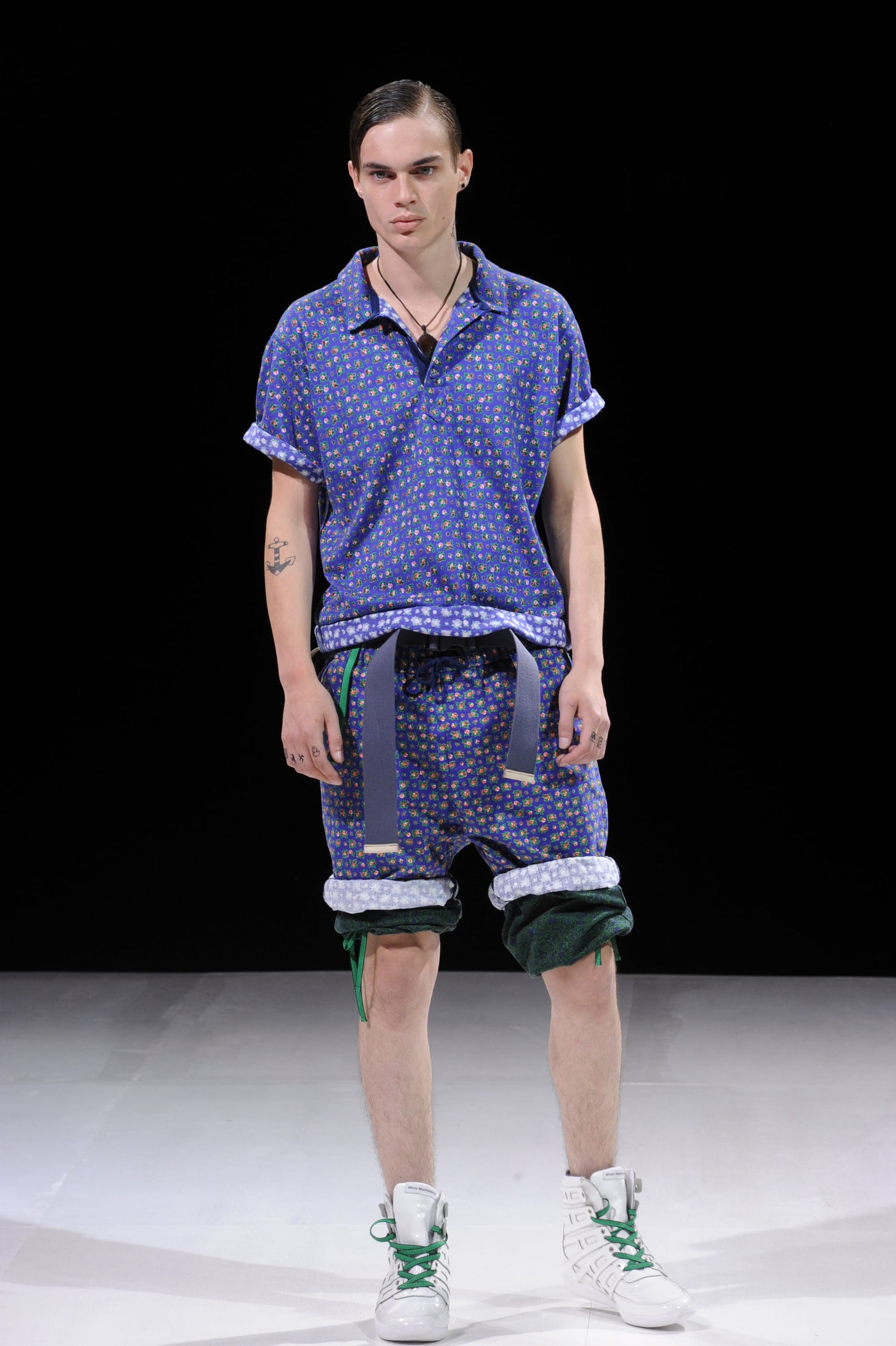 Model in a blue dotted short-sleeve shirt and matching shorts layered over green trousers.