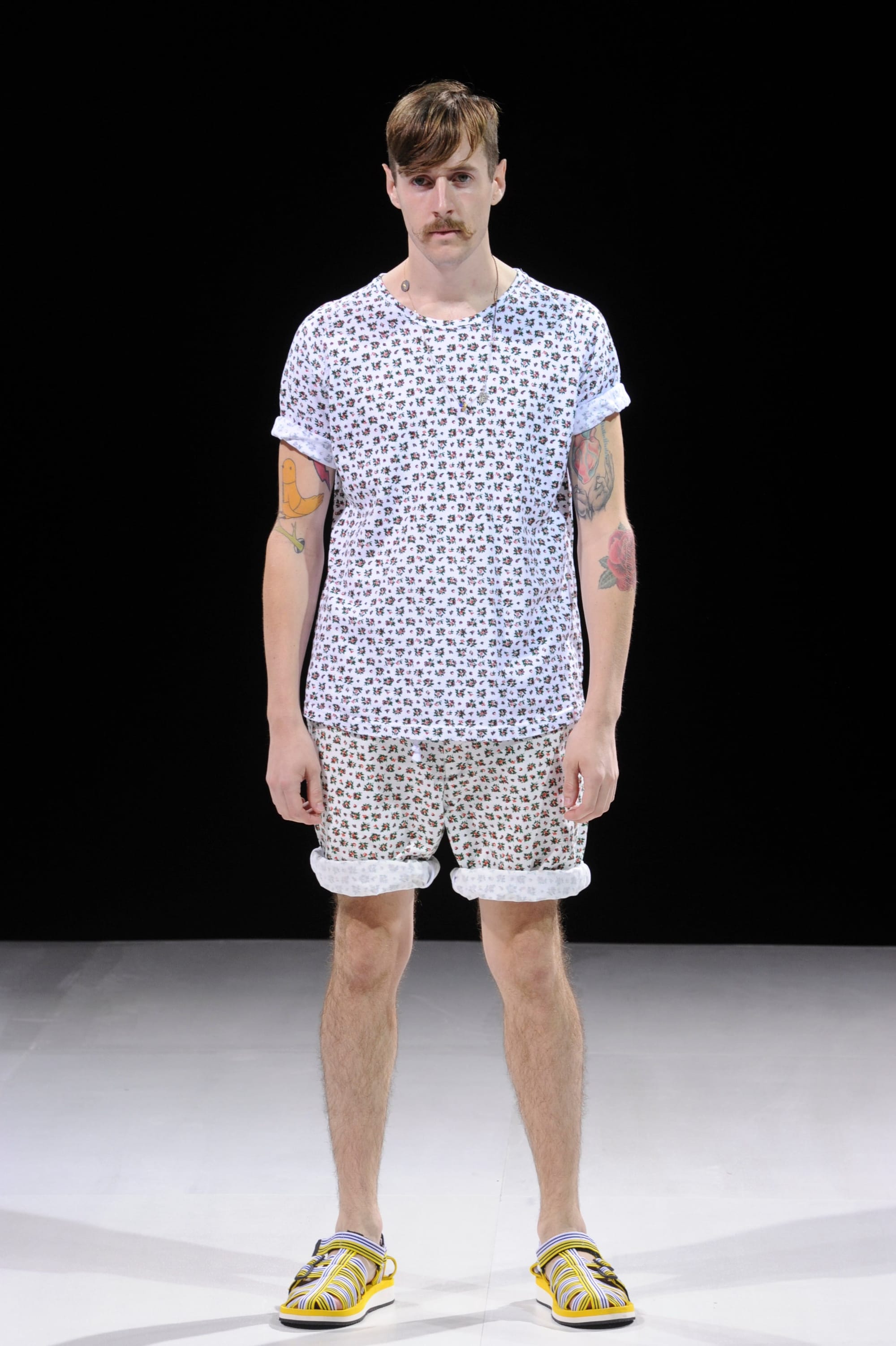 Model in a white micro-print T-shirt and matching shorts with yellow sandals.